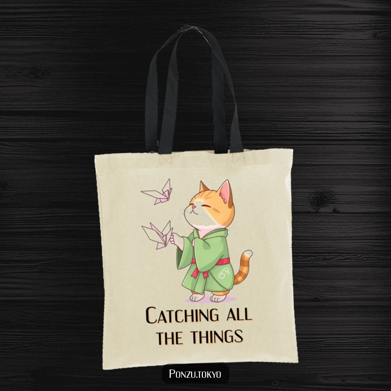 Funny cat in a green kimono playfully attempting to catch a floating origami crane on a tote bag.